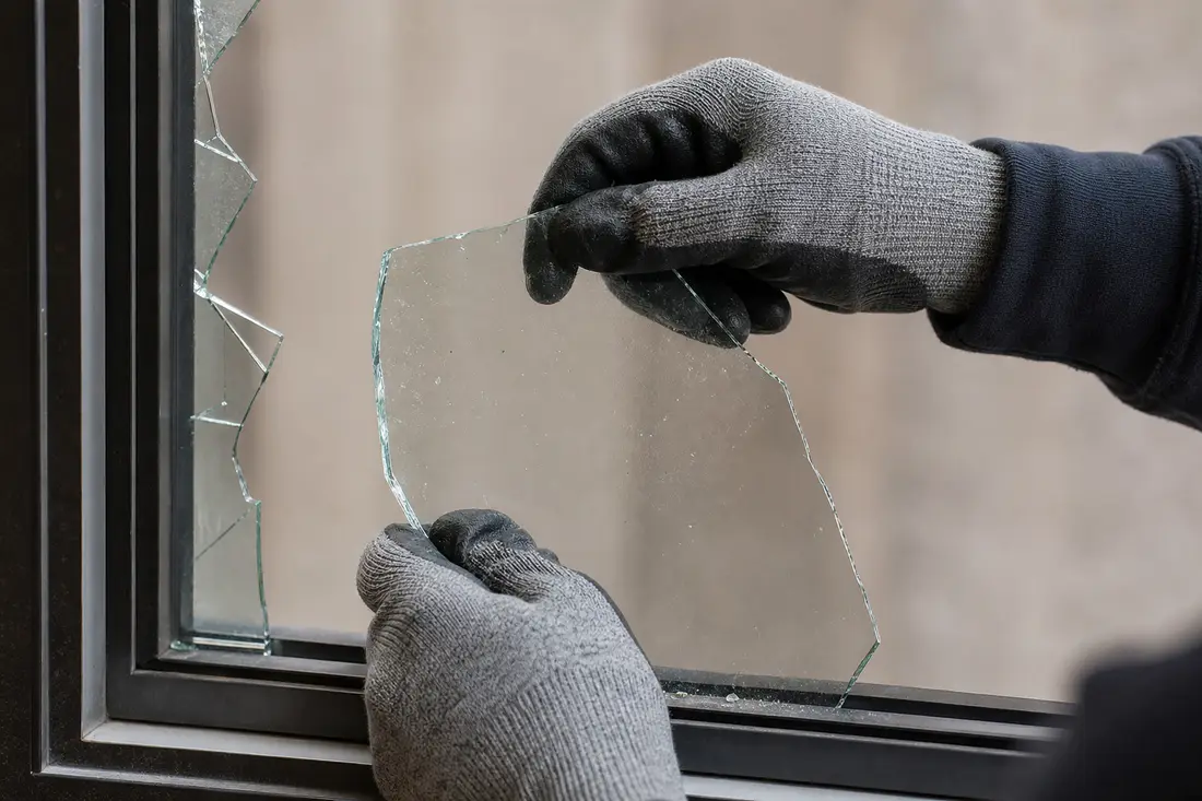 Person mit Schutzhandschuhen entfernt vorsichtig grosse Glassplitter aus einem Fensterrahmen